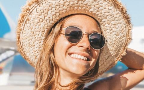 Une femme souriante portant un chapeau de soleil et des lunettes de soleil se tient devant un grand avion.