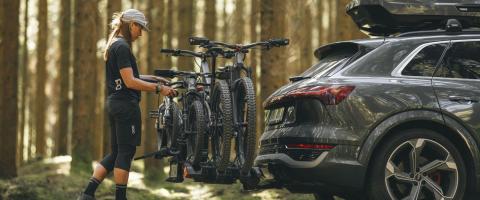 Jonge vrouw monteert vier mountainbikes op een Thule fietsendrager Une jeune femme monte quatre VTT sur un porte-vélos Thule
