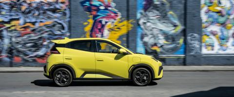 Profil latéral de la BYD Dolphin Surf jaune circulant devant un mur de graffitis.