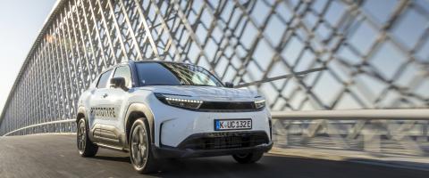 Prototype d’un SUV électrique blanc roulant sur un pont moderne, avec la mention 'PROTOTYPE' inscrite sur la portière et une plaque d’immatriculation allemande."