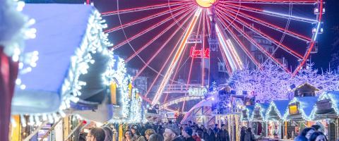 Kerstmarkten kerstkraampjes in het wit met fonkelende lampjes en reuzenrad op de achtergrond