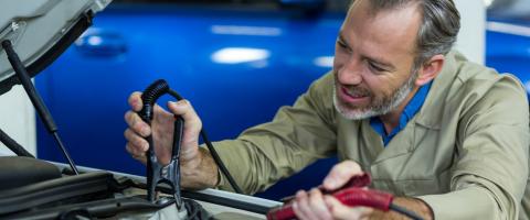 Mécanicien plaçant des câbles sur une batterie de voiture dans un garage.