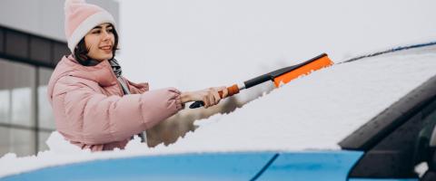 Hiver: femme en train de retirer la neige de sa voiture avec une brosse.