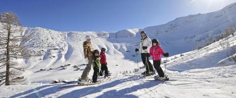 Famille avec trois enfants faisant du ski dans un paysage hivernal.