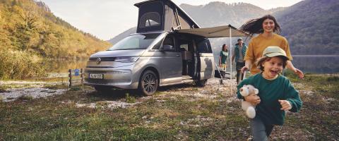 Camping: un van aménagé en pleine nature avec une jeune fille et un petit garçon en train de courir.