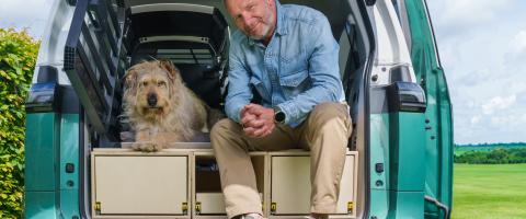 man zit naast hond in de kofferbak van een auto
