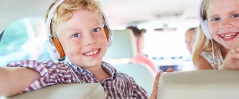 twee lachende kinderen met hoofdtelefoons op op de achterbank van een auto