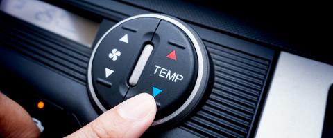 Main réglant la commande automatique de climatisation sur le tableau de bord d’une voiture.