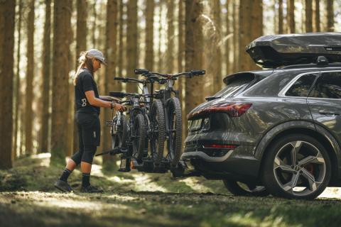 Jonge vrouw monteert vier mountainbikes op een Thule fietsendrager Une jeune femme monte quatre VTT sur un porte-vélos Thule