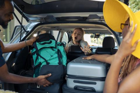 Charger sa voiture avant un départ en vacances avec famille et amis, bagages dans le coffre.