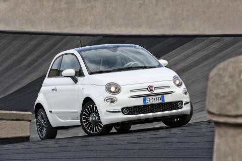 Fiat 500 blanche à l'arrêt sur un sol noir et sur fond de béton.