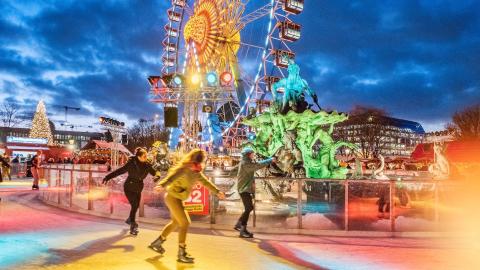 Marché de Noël: image festive de patineurs sur une piste autour d'une grande roue éclairée et d'illuminations de Noël.