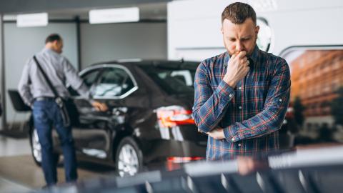 Occasion : acheteur hésitant devant une voiture dans un showroom.