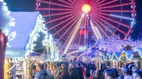 Kerstmarkten kerstkraampjes in het wit met fonkelende lampjes en reuzenrad op de achtergrond