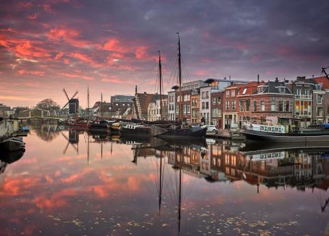 stad aan het water met oude schepen en een windmolen bij zonsondergang