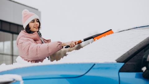 Hiver: femme en train de retirer la neige de sa voiture avec une brosse.
