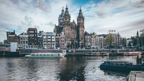 Amsterdam canal avec des bateaux touristiques et une église en arrière-plan.