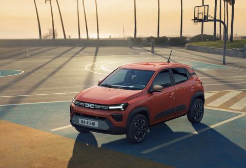 Voitures électriques: la Dacia Spring rouge sur un terrain de basket au coucher du soleil.