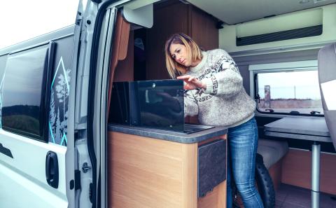 Jonge vrouw die de keuken van een camper schoonmaakt met een doekje.