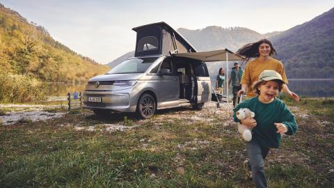 Camping: un van aménagé en pleine nature avec une jeune fille et un petit garçon en train de courir.