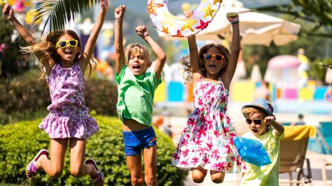 4 enfants qui crient et applaudissent, vêtus de tenues colorées, près d'une piscine
