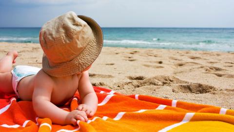 baby met hoedje op een badhanddoek op het strand