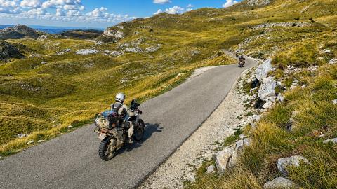 Motard circulant sur une route étroite de montagne entourée de verdure.