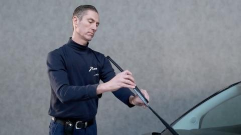 Un homme vérifie les essuie-glaces d'une voiture foncée.
