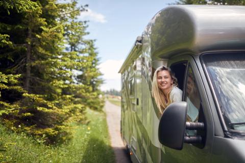 Une jeune femme blonde se penche par la fenêtre d'un camping-car.
