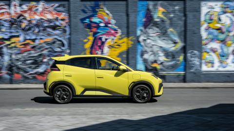 Profil latéral de la BYD Dolphin Surf jaune circulant devant un mur de graffitis.