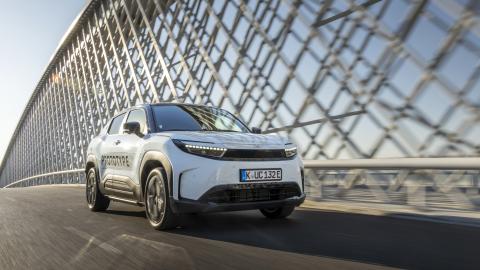 Prototype d’un SUV électrique blanc roulant sur un pont moderne, avec la mention 'PROTOTYPE' inscrite sur la portière et une plaque d’immatriculation allemande."